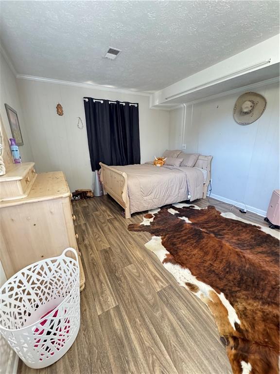 bedroom with visible vents, crown molding, a textured ceiling, and wood finished floors