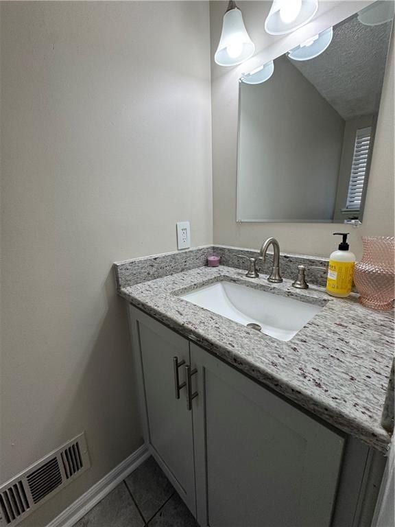 bathroom featuring a textured ceiling, vanity, baseboards, visible vents, and tile patterned floors