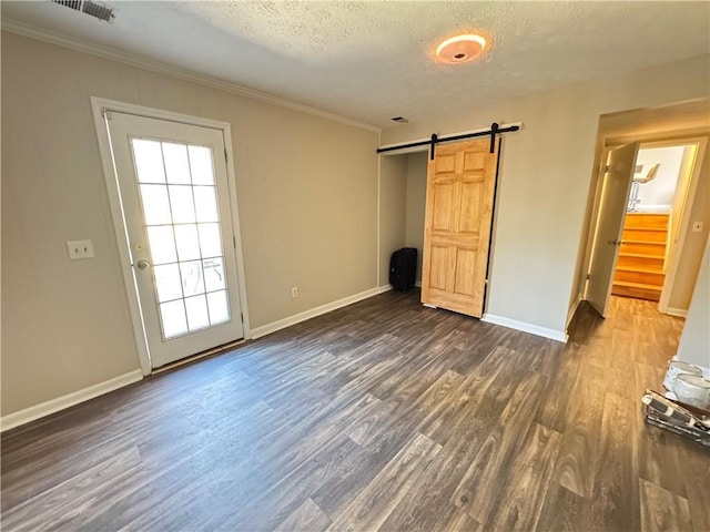 unfurnished bedroom featuring visible vents, a barn door, dark wood-type flooring, ornamental molding, and a textured ceiling