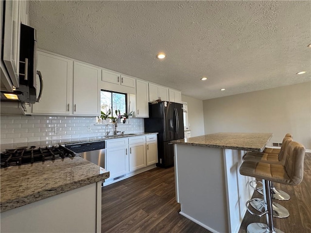 kitchen featuring dark wood-style floors, freestanding refrigerator, a sink, white cabinetry, and backsplash