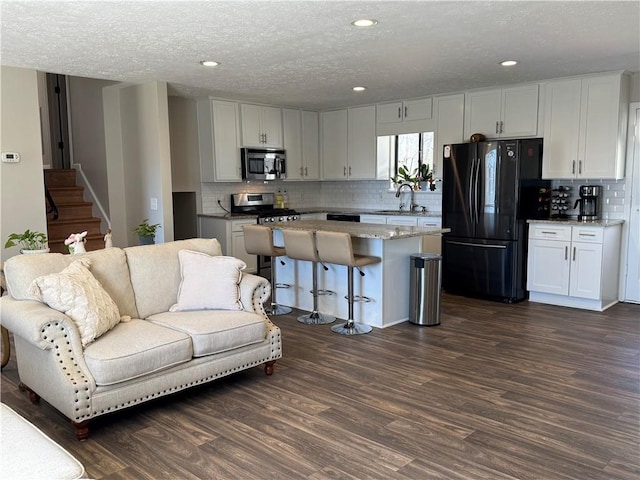 kitchen with stainless steel appliances, a kitchen island, a sink, white cabinetry, and dark wood finished floors