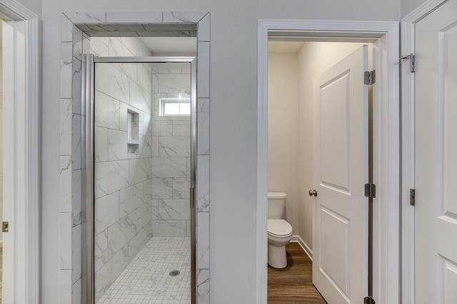 bathroom with toilet, a marble finish shower, and wood finished floors