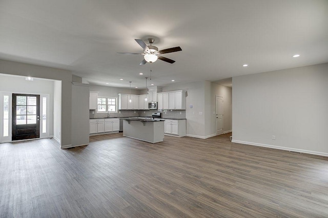 kitchen featuring dark countertops, stainless steel microwave, open floor plan, and decorative backsplash