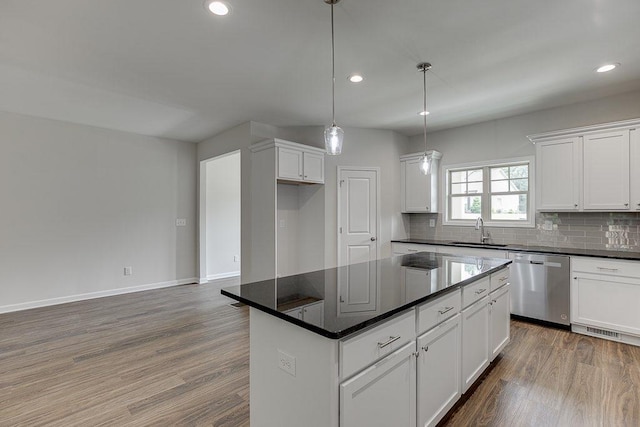 kitchen featuring dark countertops, decorative backsplash, stainless steel dishwasher, a sink, and wood finished floors