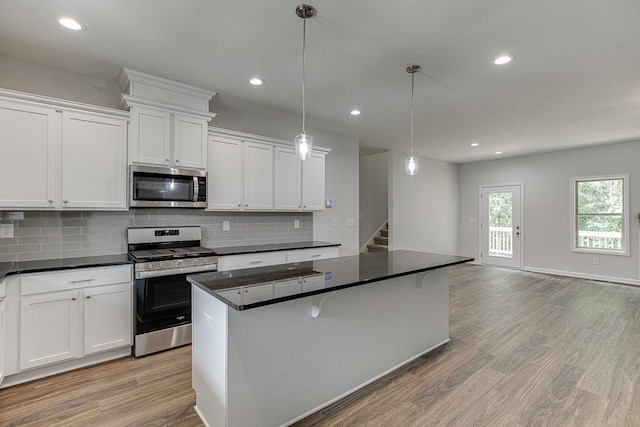 kitchen with dark countertops, light wood finished floors, a kitchen island, and appliances with stainless steel finishes