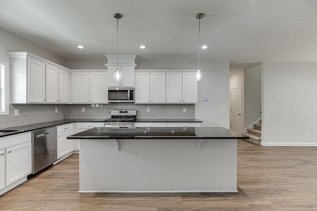 kitchen featuring decorative light fixtures, appliances with stainless steel finishes, white cabinetry, a kitchen island, and light wood-type flooring