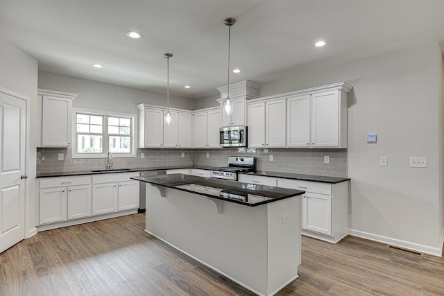 kitchen with dark countertops, appliances with stainless steel finishes, a sink, and wood finished floors