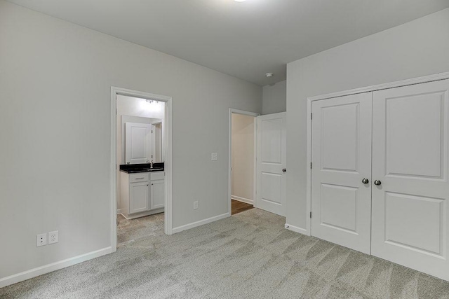 unfurnished bedroom with a closet, light colored carpet, baseboards, and ensuite bathroom