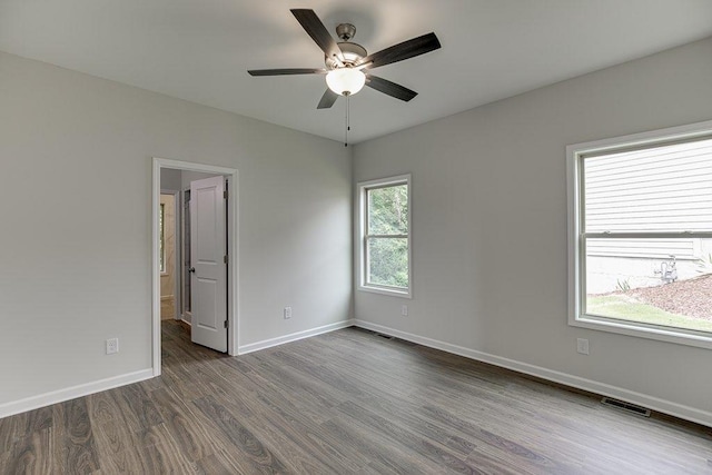 spare room featuring dark wood-style floors, a ceiling fan, visible vents, and baseboards