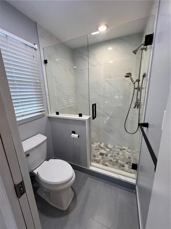 bathroom featuring a shower with shower door and toilet