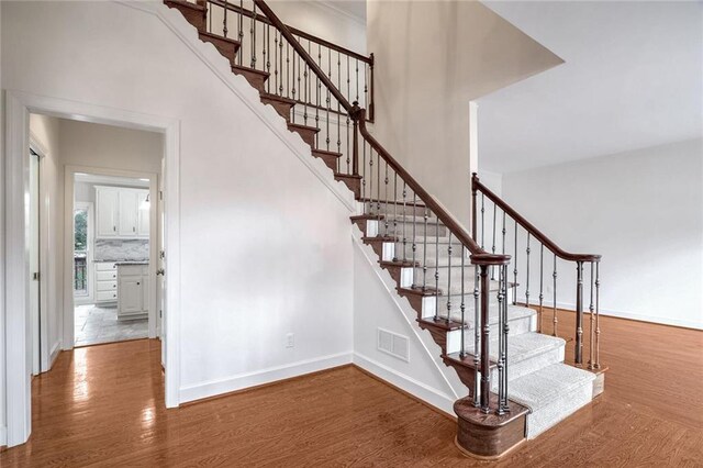 stairs featuring a towering ceiling and wood-type flooring