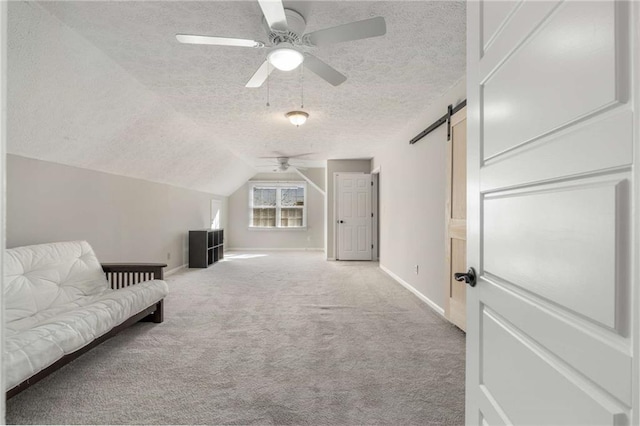 interior space with lofted ceiling, light colored carpet, ceiling fan, a barn door, and a textured ceiling