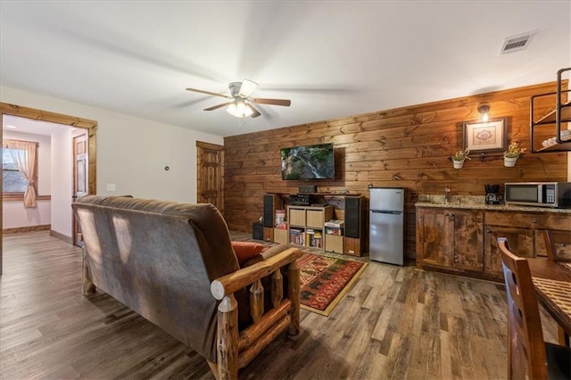 living room featuring hardwood / wood-style flooring, ceiling fan, and wooden walls