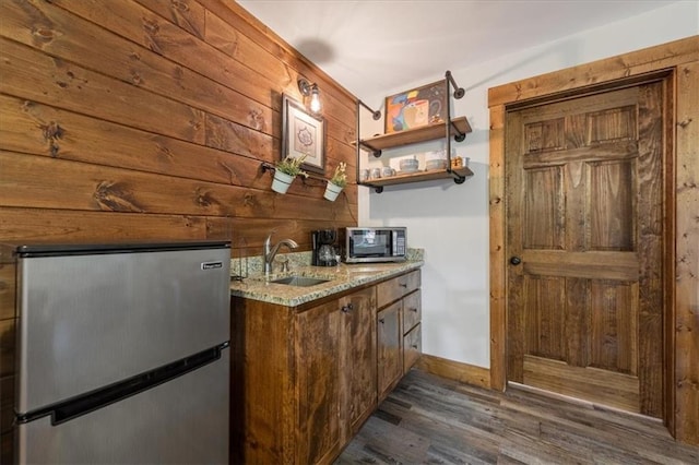 bar featuring appliances with stainless steel finishes, dark wood-type flooring, sink, wood walls, and light stone counters