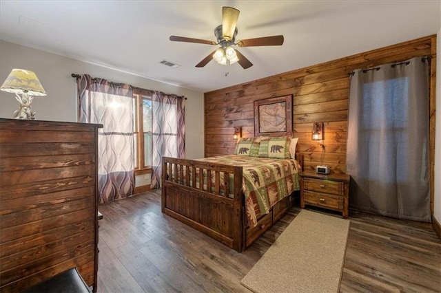 bedroom with ceiling fan, wooden walls, and dark wood-type flooring