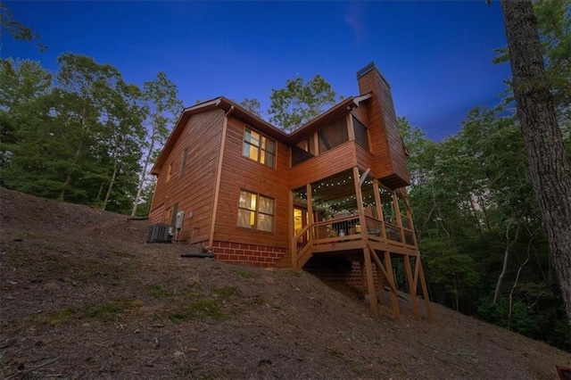 back house at dusk featuring a wooden deck and central AC