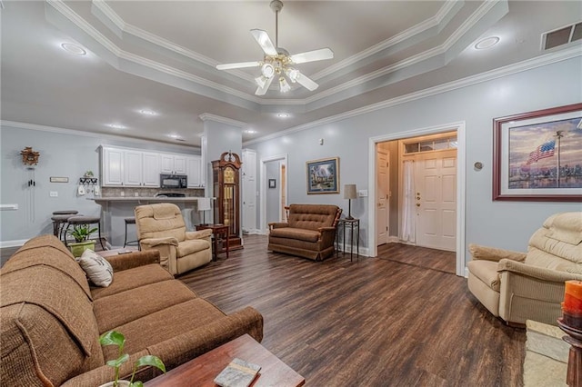 living room with crown molding, a tray ceiling, dark hardwood / wood-style floors, and ceiling fan