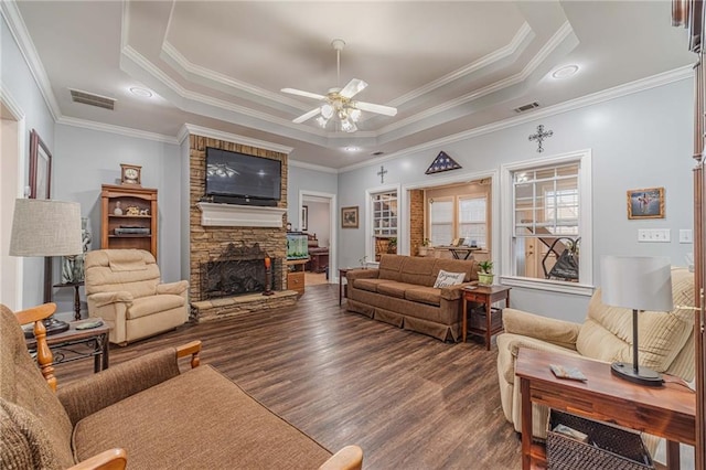 living room with dark wood-type flooring, a stone fireplace, crown molding, a raised ceiling, and ceiling fan