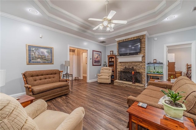 living room with ceiling fan, wood-type flooring, a tray ceiling, and a stone fireplace