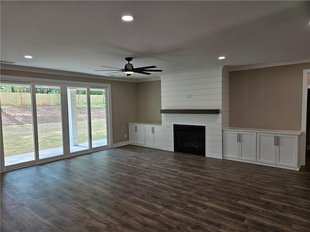 unfurnished living room featuring a large fireplace, a ceiling fan, and dark wood finished floors