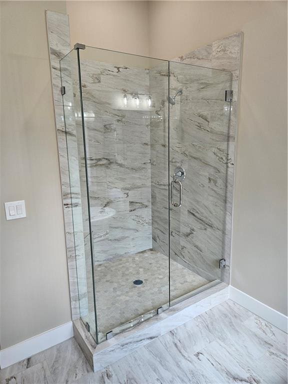 full bath featuring marble finish floor, baseboards, and a stall shower