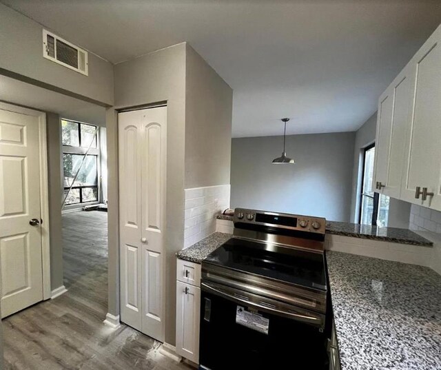 kitchen with light wood-type flooring, stone countertops, white cabinetry, black electric range oven, and tasteful backsplash