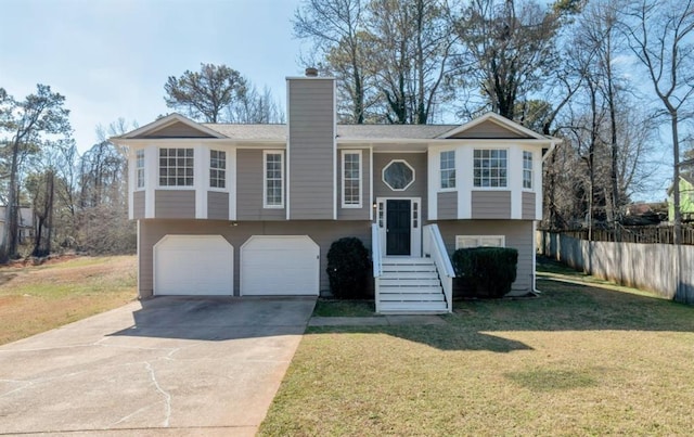 bi-level home with fence, a front yard, a chimney, driveway, and an attached garage