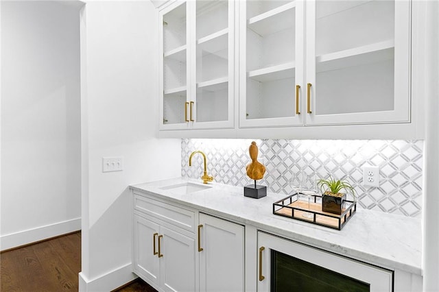 bar with sink, light stone counters, tasteful backsplash, white cabinets, and dark wood-type flooring