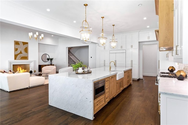 kitchen with a large island, built in appliances, sink, white cabinets, and dark wood-type flooring