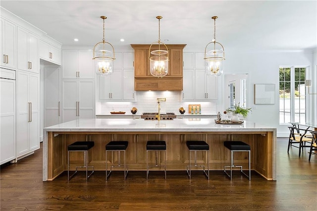 kitchen with dark wood-type flooring, white cabinetry, decorative light fixtures, and an island with sink