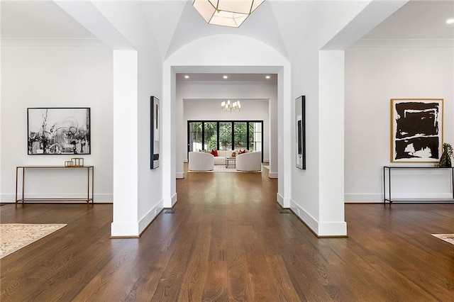 hallway with ornamental molding, a chandelier, dark hardwood / wood-style floors, and vaulted ceiling