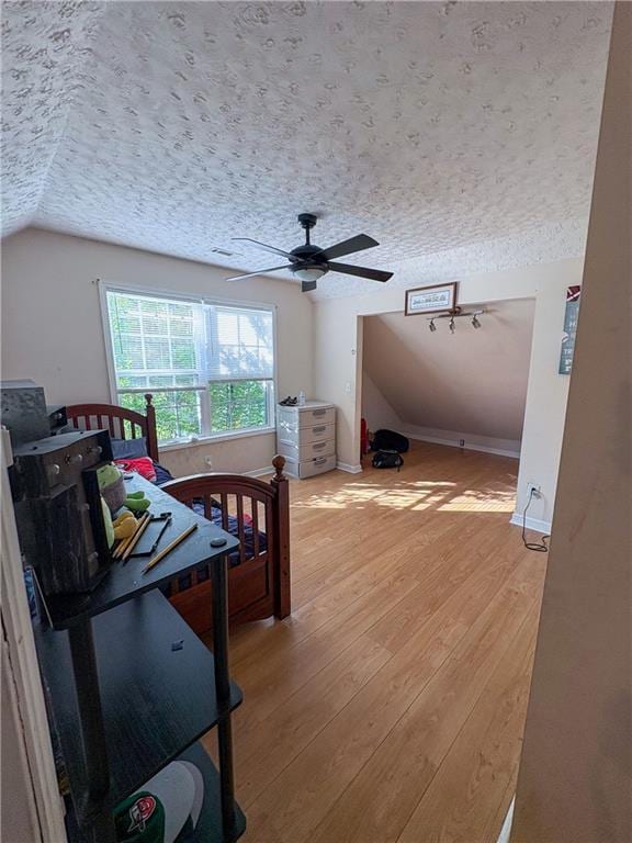 bedroom with light wood-style floors, a textured ceiling, a ceiling fan, baseboards, and vaulted ceiling