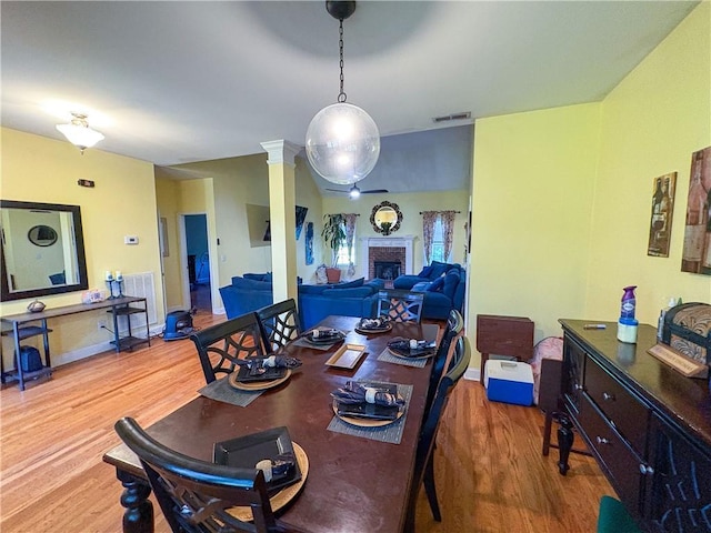 dining room with a fireplace, a ceiling fan, wood finished floors, ornate columns, and visible vents