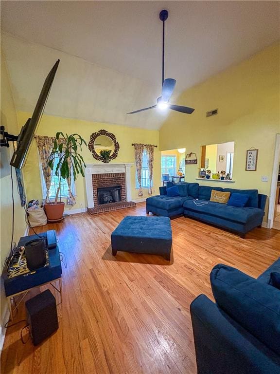 living area with ceiling fan, visible vents, a brick fireplace, wood finished floors, and high vaulted ceiling