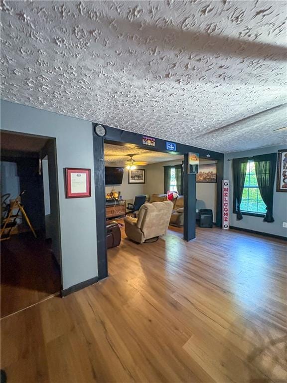 living room with baseboards, ceiling fan, a textured ceiling, and wood finished floors