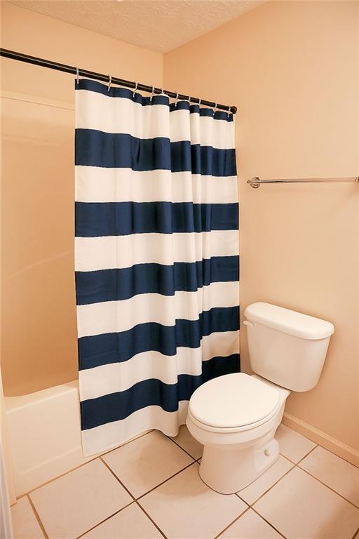 bathroom featuring toilet, tile patterned floors, baseboards, and a textured ceiling