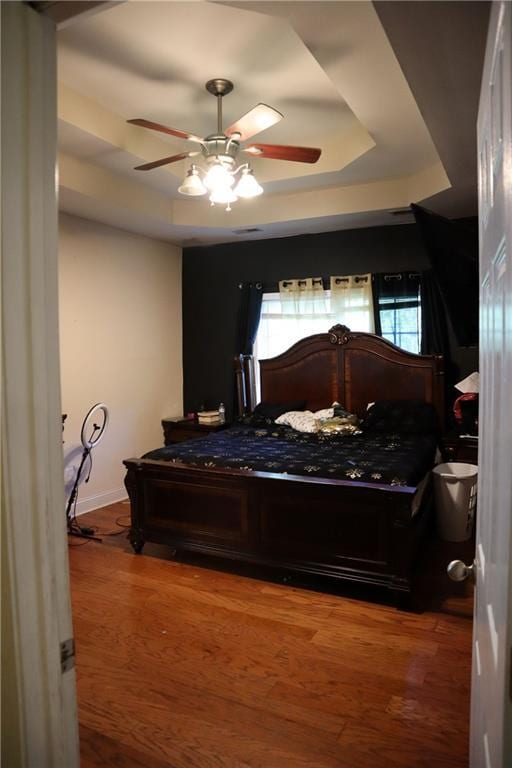 bedroom featuring a ceiling fan, wood finished floors, and a tray ceiling