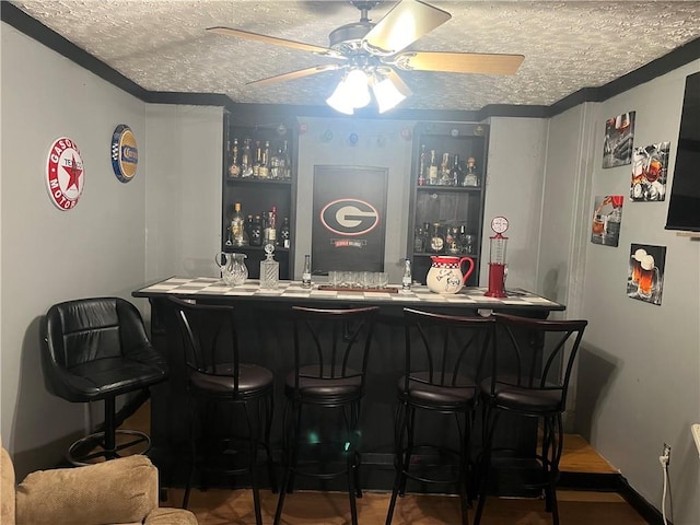 bar with a ceiling fan, a textured ceiling, baseboards, and wet bar
