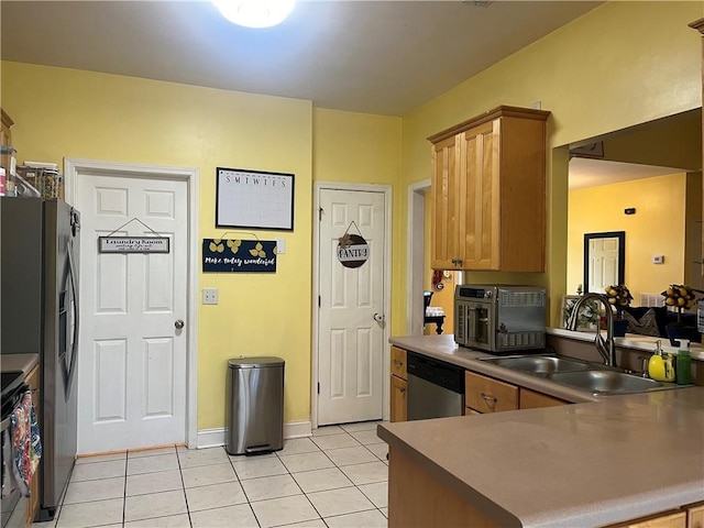 kitchen featuring brown cabinetry, a peninsula, light tile patterned flooring, a sink, and appliances with stainless steel finishes