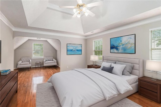 bedroom with a raised ceiling, light wood finished floors, and multiple windows