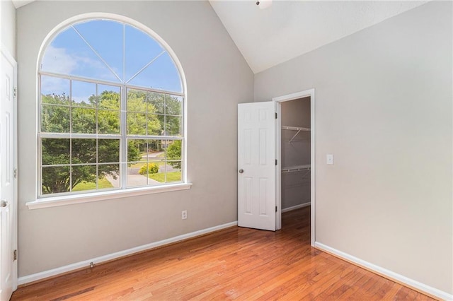 unfurnished bedroom with a spacious closet, lofted ceiling, multiple windows, and light wood finished floors