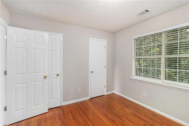 unfurnished bedroom featuring baseboards, a textured ceiling, wood finished floors, and visible vents