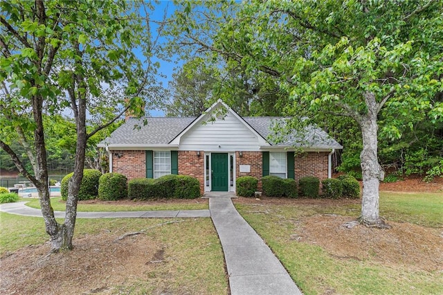 view of front of home featuring roof with shingles, a front yard, and brick siding