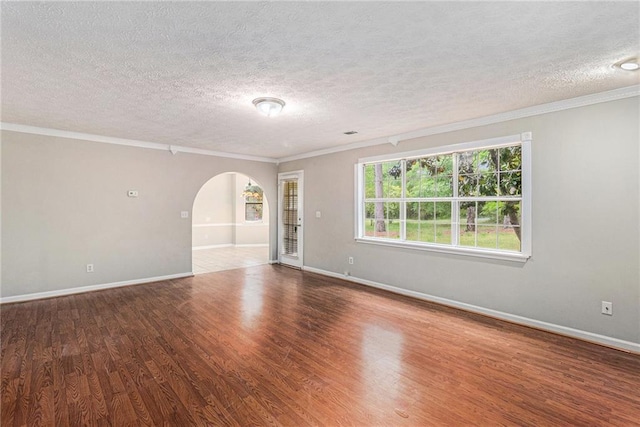 empty room with arched walkways, a textured ceiling, and ornamental molding