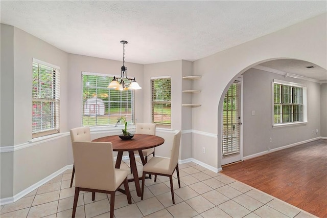 dining area with an inviting chandelier, arched walkways, baseboards, and light tile patterned flooring