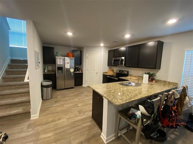 kitchen featuring sink, kitchen peninsula, a breakfast bar, appliances with stainless steel finishes, and light wood-type flooring