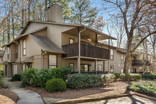 exterior space featuring a ceiling fan, a balcony, roof with shingles, and a chimney