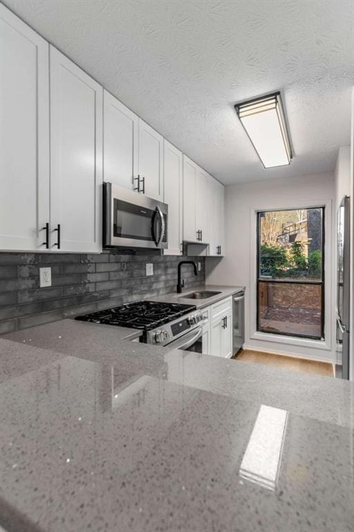 kitchen with light stone countertops, a sink, stainless steel appliances, white cabinetry, and tasteful backsplash