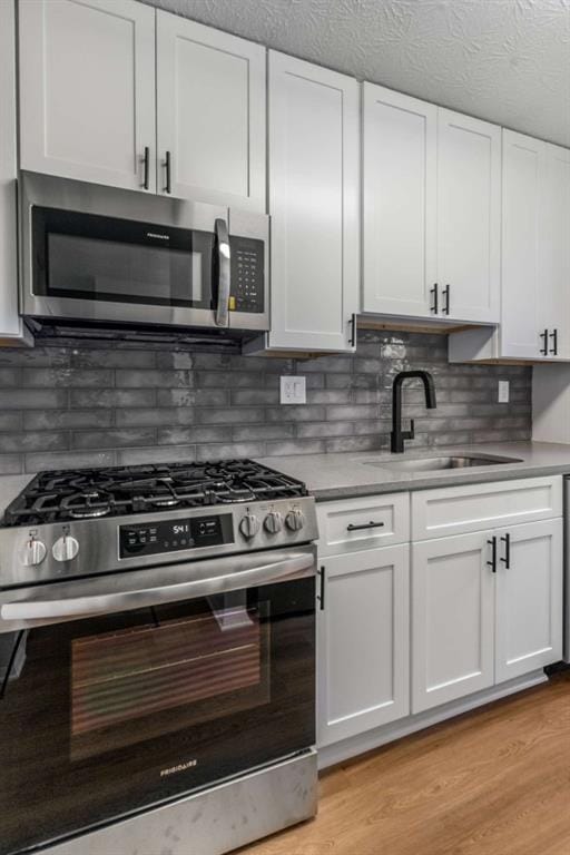 kitchen featuring a sink, light wood-style floors, appliances with stainless steel finishes, white cabinetry, and backsplash