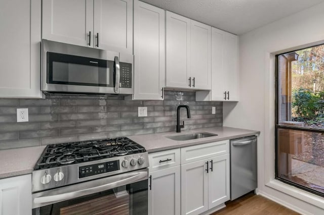 kitchen featuring a sink, tasteful backsplash, white cabinetry, stainless steel appliances, and light countertops